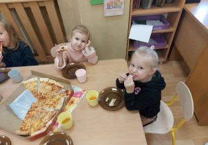 Dzieci siedzą przy stole i jedzą pizze
